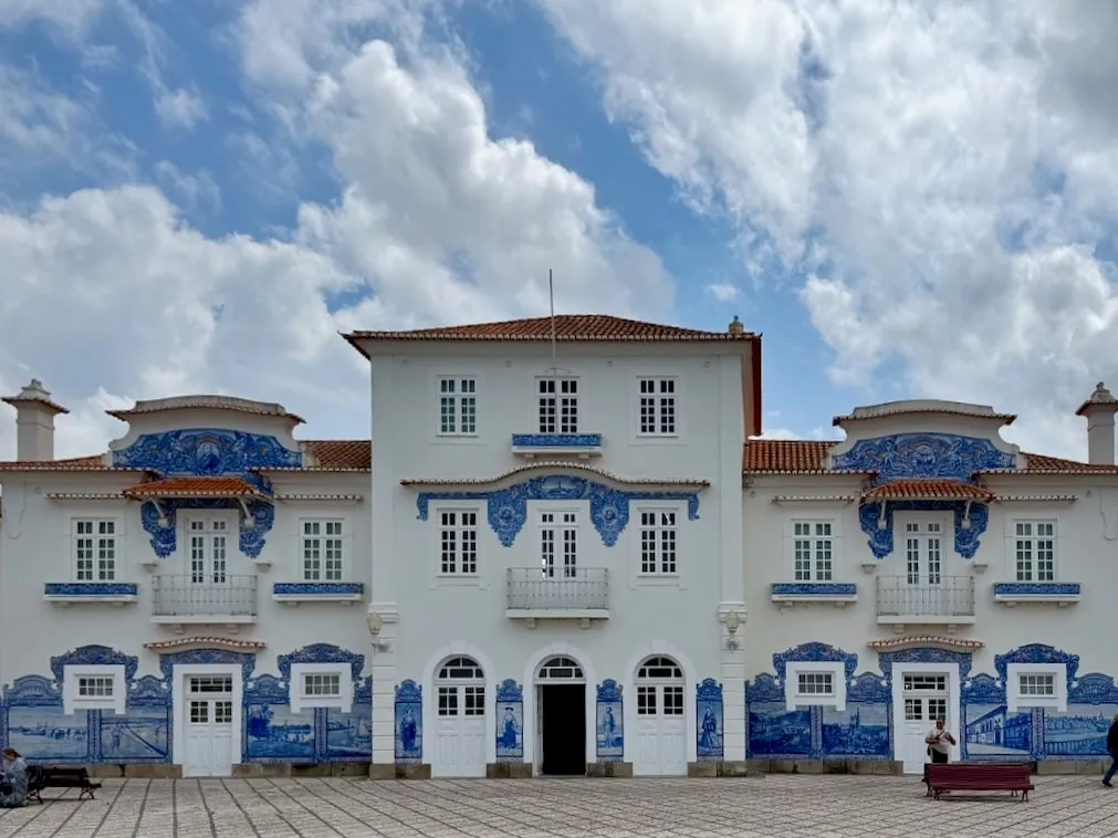 Aveiro's historic railway station building, white with blue and white azulejo tile panels, under a cloudy sky.